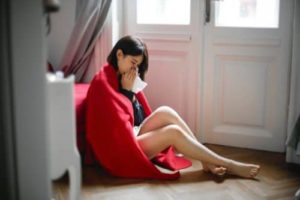 Young woman sitting on the ground sneezing