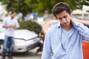 Man holds neck in pain and stands in front of car accident scene