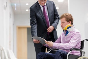 an injured man in a wheelchair is signing documents with a male attorney