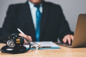 A stethoscope and a gavel in the foreground with a medical malpractice lawyer in New Haven working on a case on their laptop in the background.