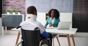 A man in a wheelchair with a neck brace and his arm in a sling consulting with a catastrophic injury lawyer in Hartford.