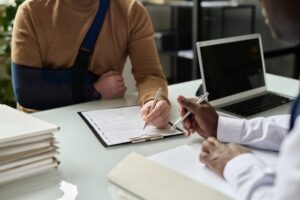 A man with an arm injury is filling out documents at a Waterbury catastrophic injury lawyer.