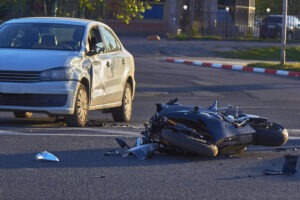 An injured man with an arm sling and foot cast sitting on a couch with his helmet, calling a motorcycle accident lawyer.