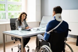 An injured man in a wheelchair, with his arm in a sling and wearing a neck brace, discussing his case with an experienced personal injury lawyer in Waterbury.