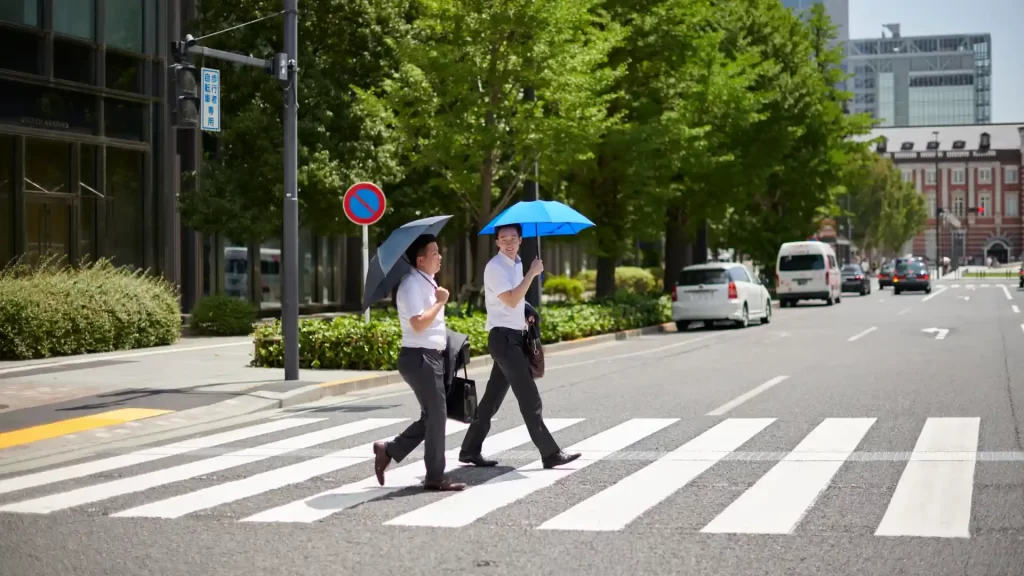 Two pedestrians with umbrellas crossing street at crosswalk