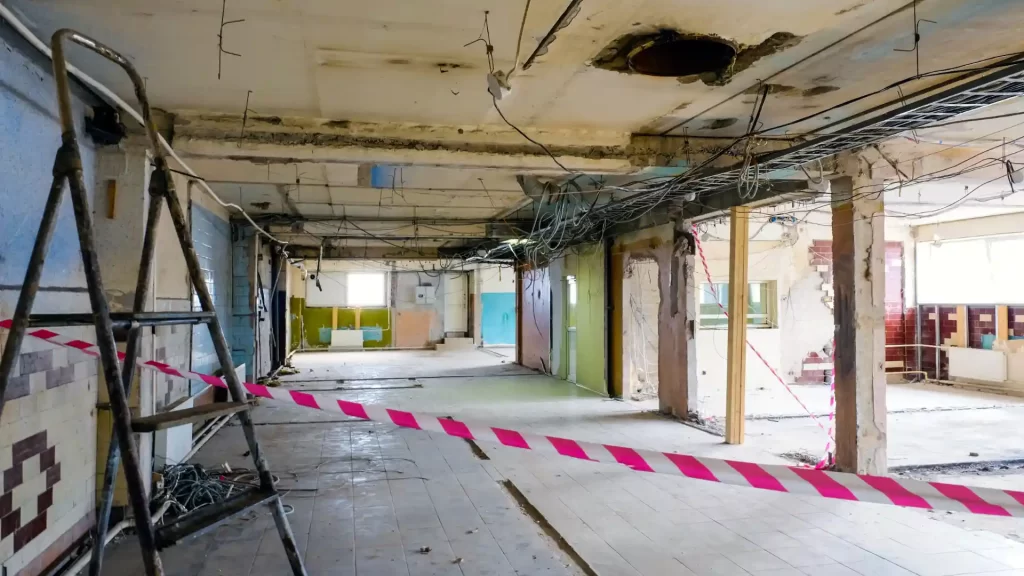 Interior de edificio abandonado con techo dañado y cinta de precaución